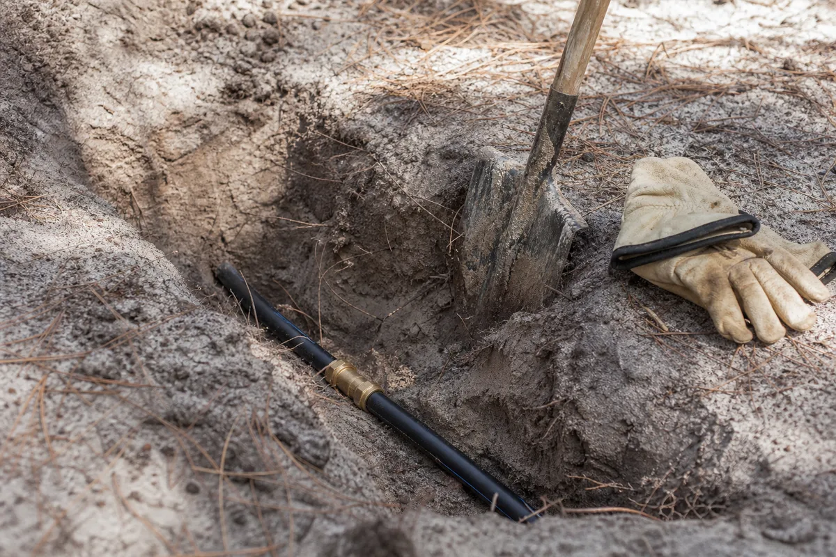 Canalisation d&rsquo;eau apparente dans une tranchée de sable landais bordée de pins